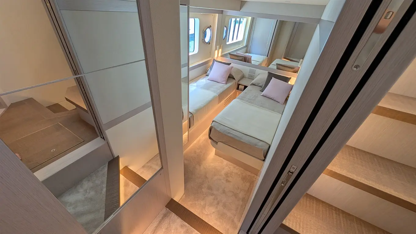 Modern two-bed cabin with large round window, soft lighting, and plush bedding, featuring wooden details and carpeted floor.