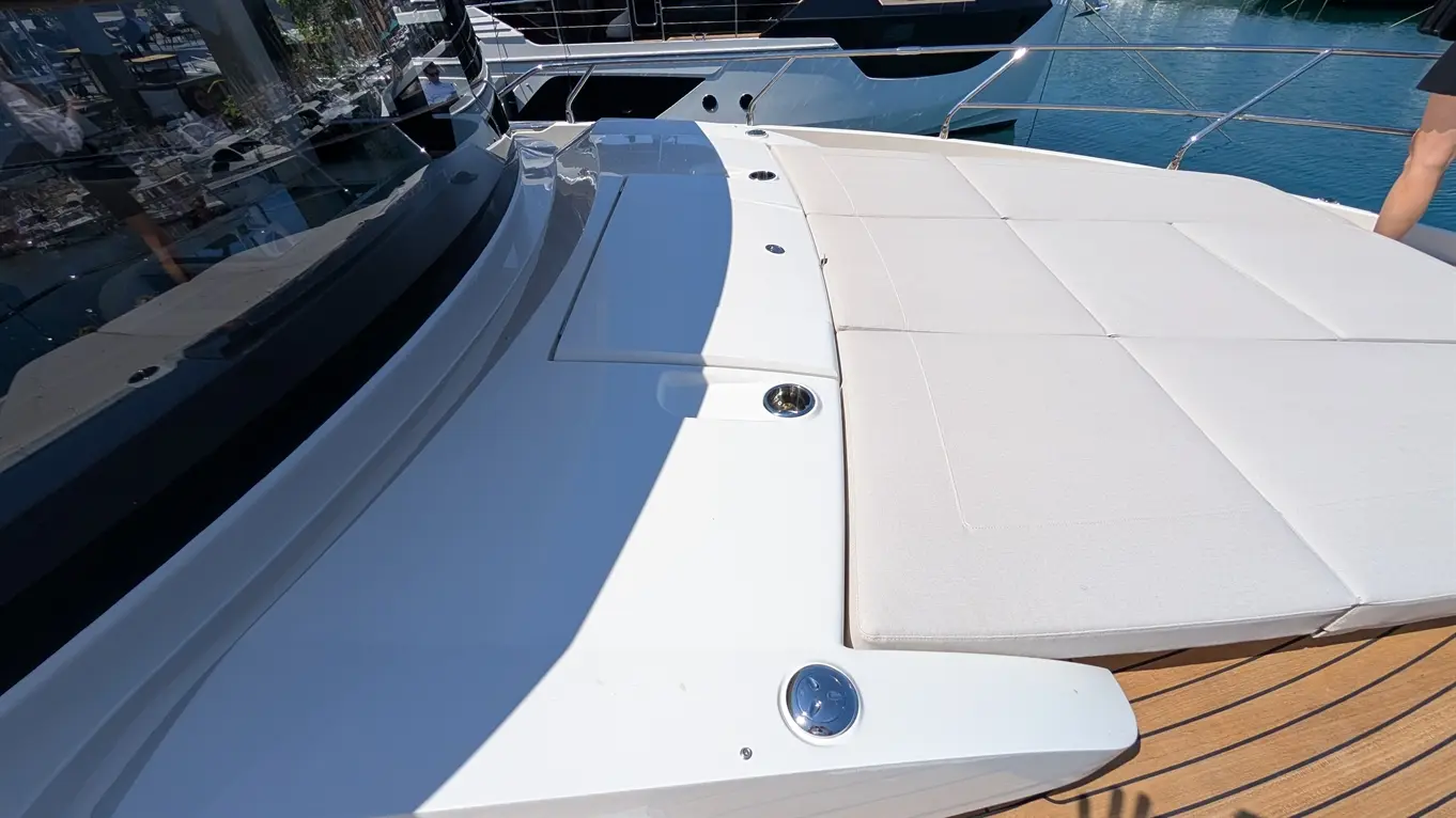 Luxury yacht deck featuring a white cushioned sunbathing area, polished surfaces, and reflections of nearby boats on the water.
