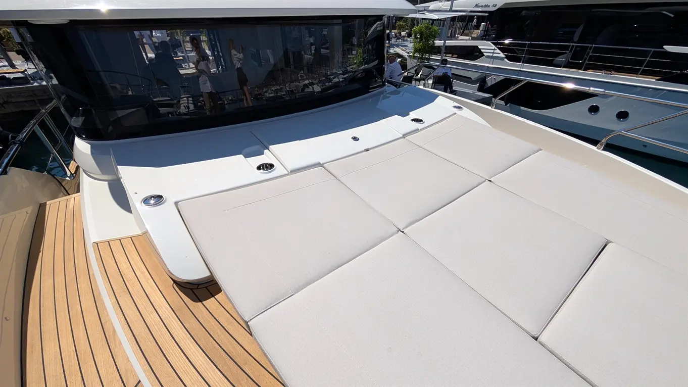 Luxury yacht deck featuring cream-coloured cushions, wooden flooring, and reflections of people and boats in the glass window.