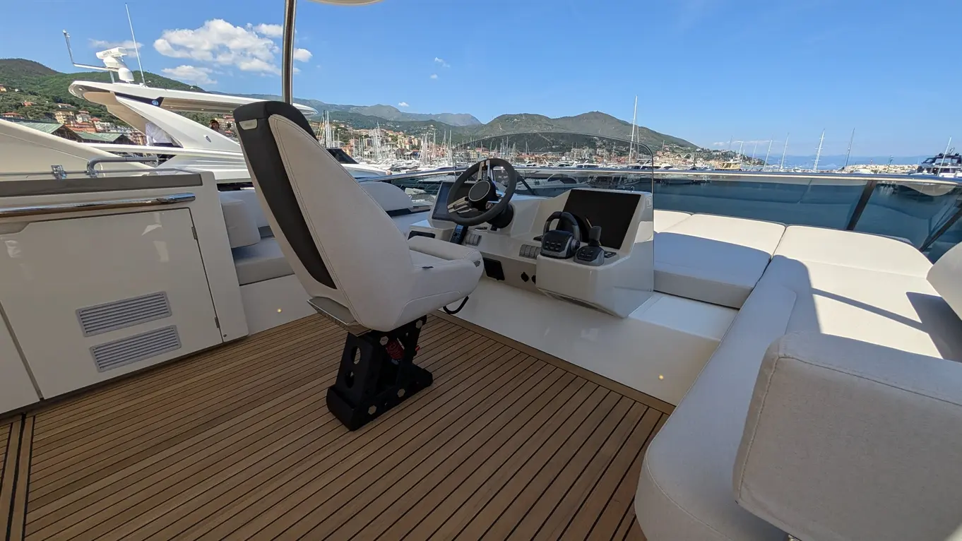 Luxury yacht cockpit interior featuring a grey captain's chair, steering wheel, and control console, with a marina view.