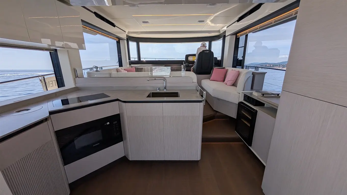Modern boat interior featuring a kitchen area, seating with pink cushions, and panoramic windows overlooking the sea.
