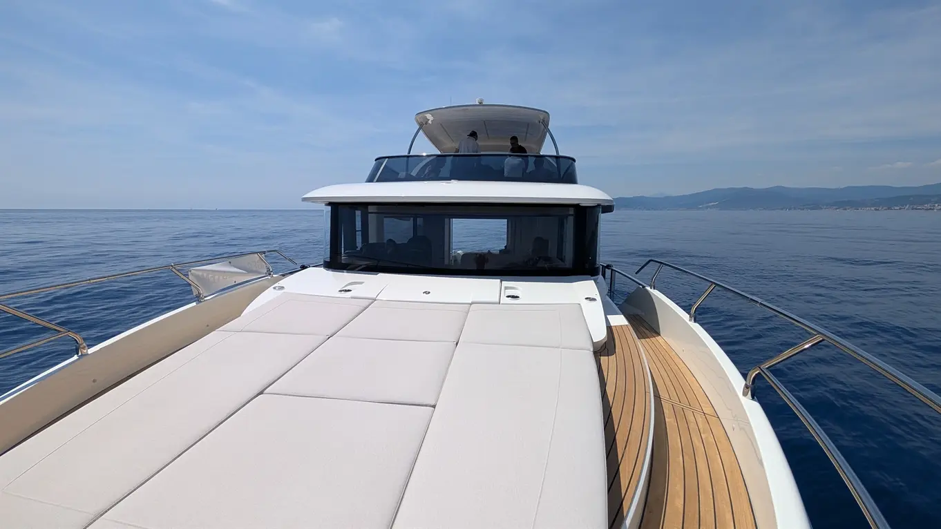 Luxury yacht deck with outdoor seating, panoramic views of calm sea and coastline, under a clear blue sky.
