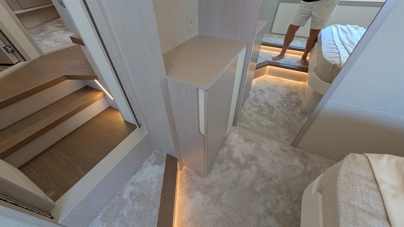 Contemporary interior of a cabin featuring soft lighting, stairs, a side table, and a bed with a plush mattress.