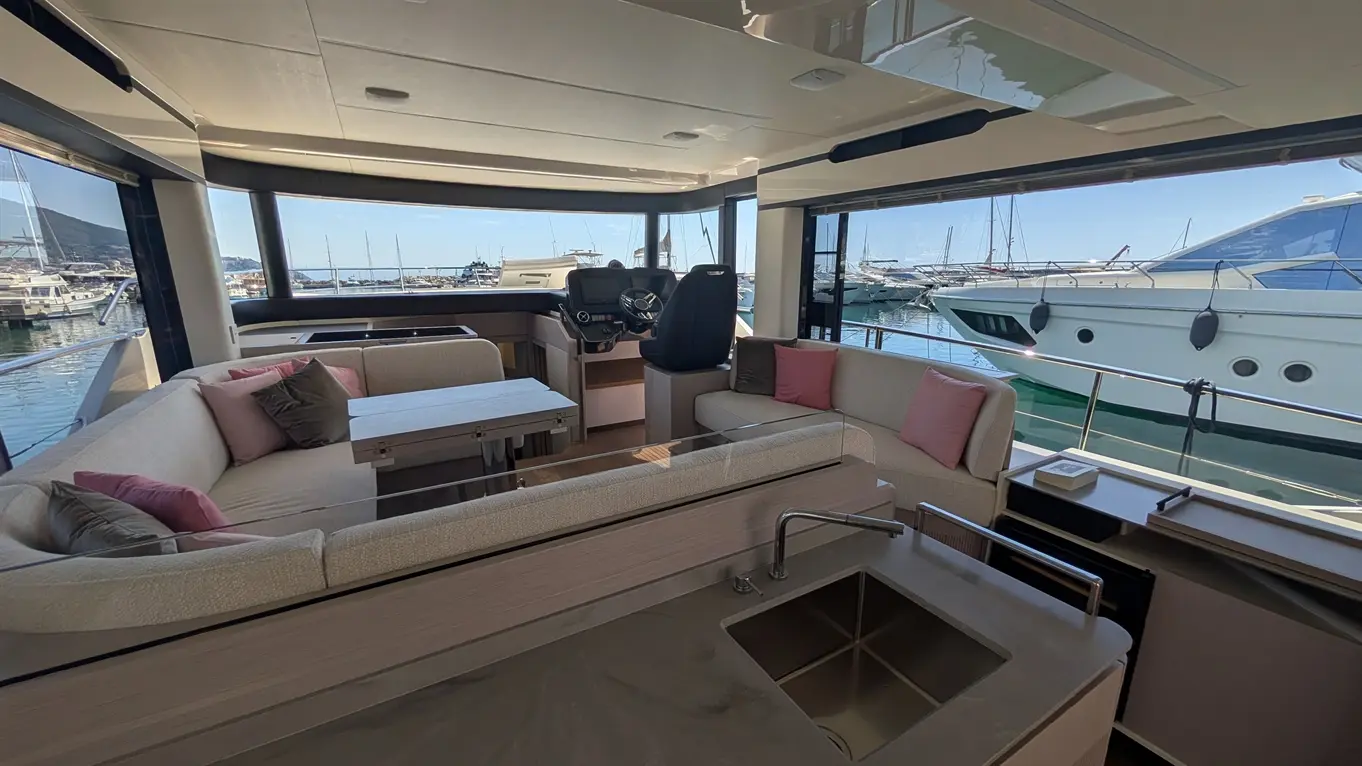 Luxury yacht interior with seating, helm station and panoramic windows overlooking a marina filled with boats.