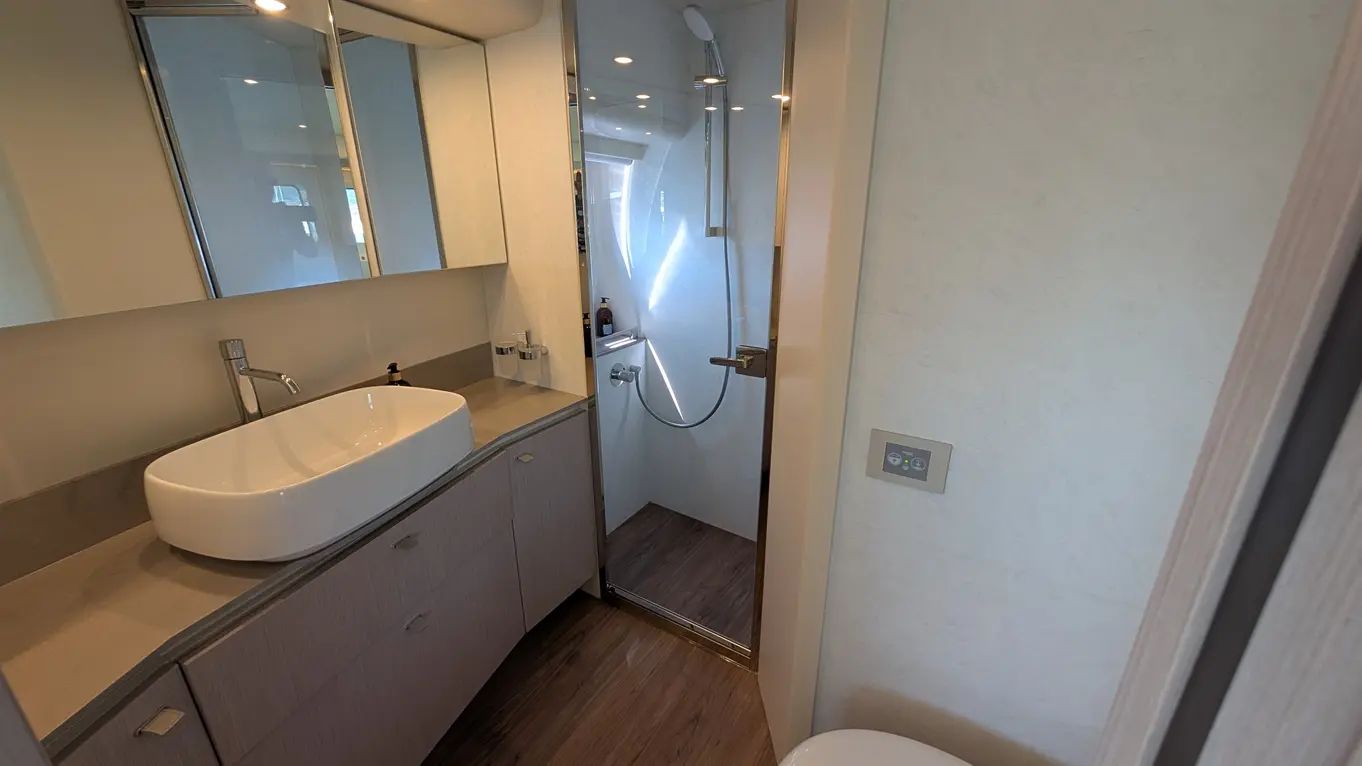 Modern bathroom featuring a large basin, shower cubicle, and sleek cabinetry with wood flooring and stylish mirror accents.
