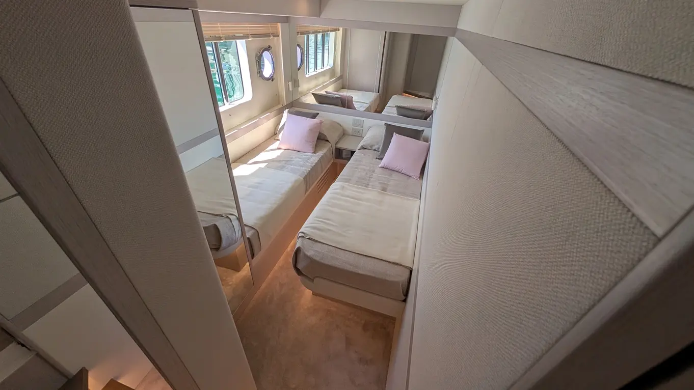 Interior view of a yacht cabin featuring two single beds with pink cushions, a mirror, and porthole windows.