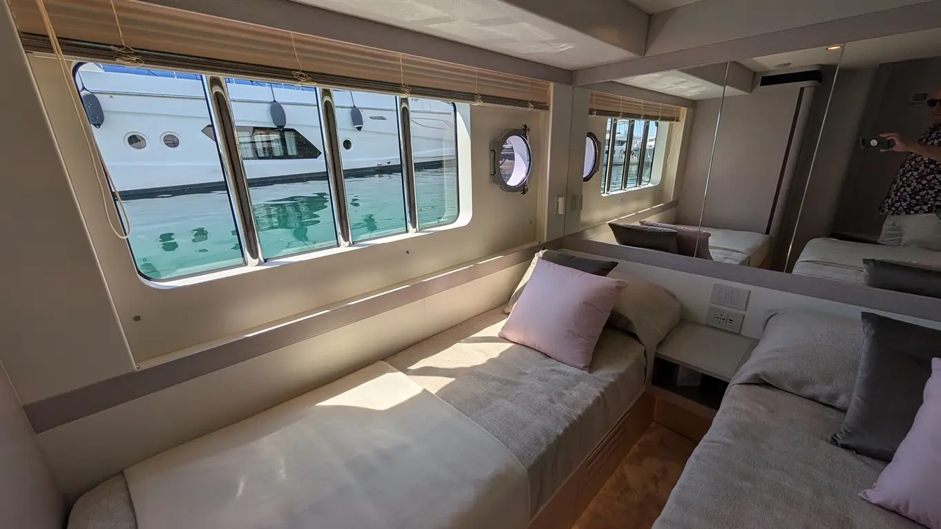 Interior of a yacht cabin with a bed, pink pillow, and large windows showcasing a view of the docked boat and water.