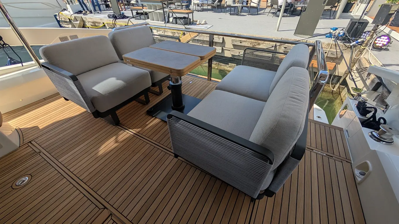 Stylish outdoor seating area with grey upholstered sofas and a wooden table on a yacht deck, surrounded by a marina view.