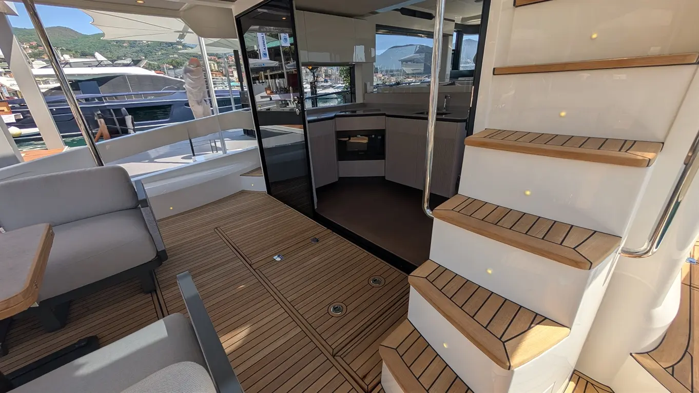 Modern yacht interior featuring a staircase, spacious seating area, and kitchenette with a view of the marina outside.
