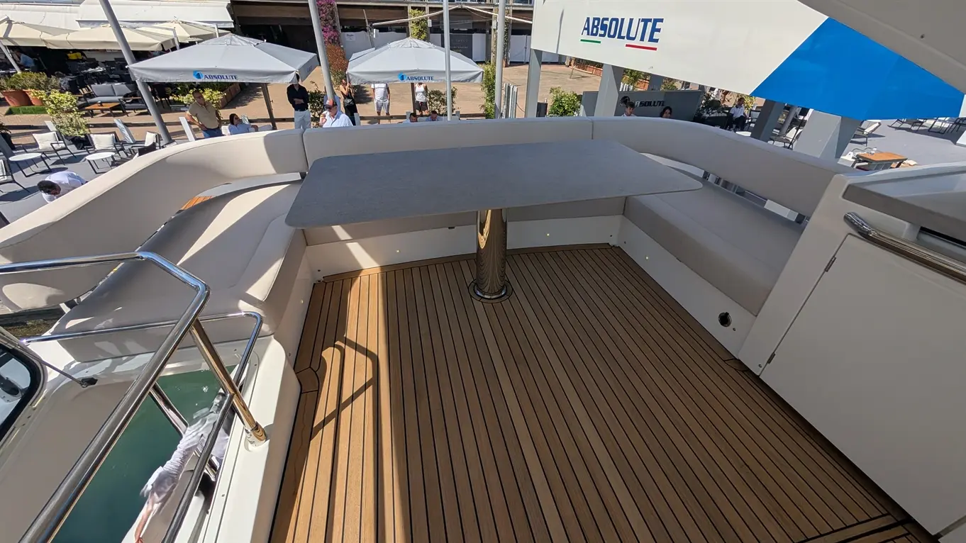 Deck area of a boat featuring a round table, cushioned seating, and wooden flooring, with an 'Absolute' sign visible above.