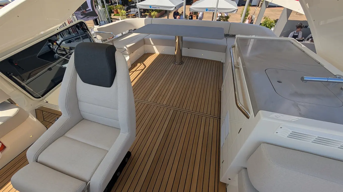 Modern boat interior showing a plush grey seat, a grey table, wooden flooring, and a scenic outdoor view.