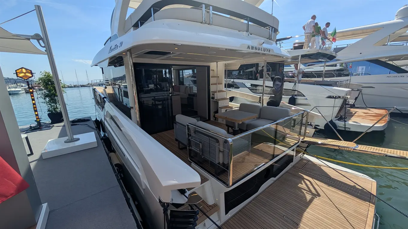 A luxurious boat with outdoor seating and wooden deck, docked at a marina on a sunny day, featuring the name "A B S O L U T E.