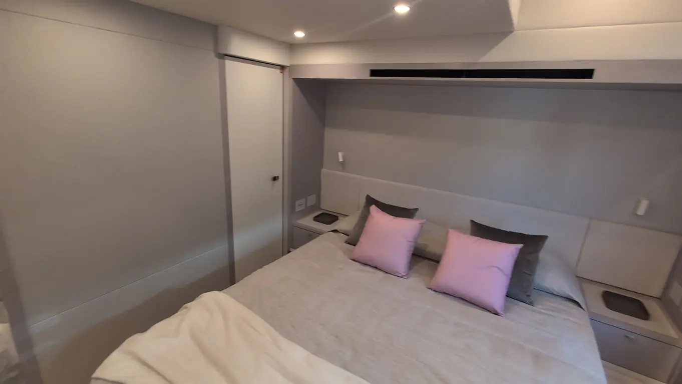 Cosy bedroom with a double bed, two pink cushions, a grey blanket, and minimalist decor, featuring a wall-mounted air vent.