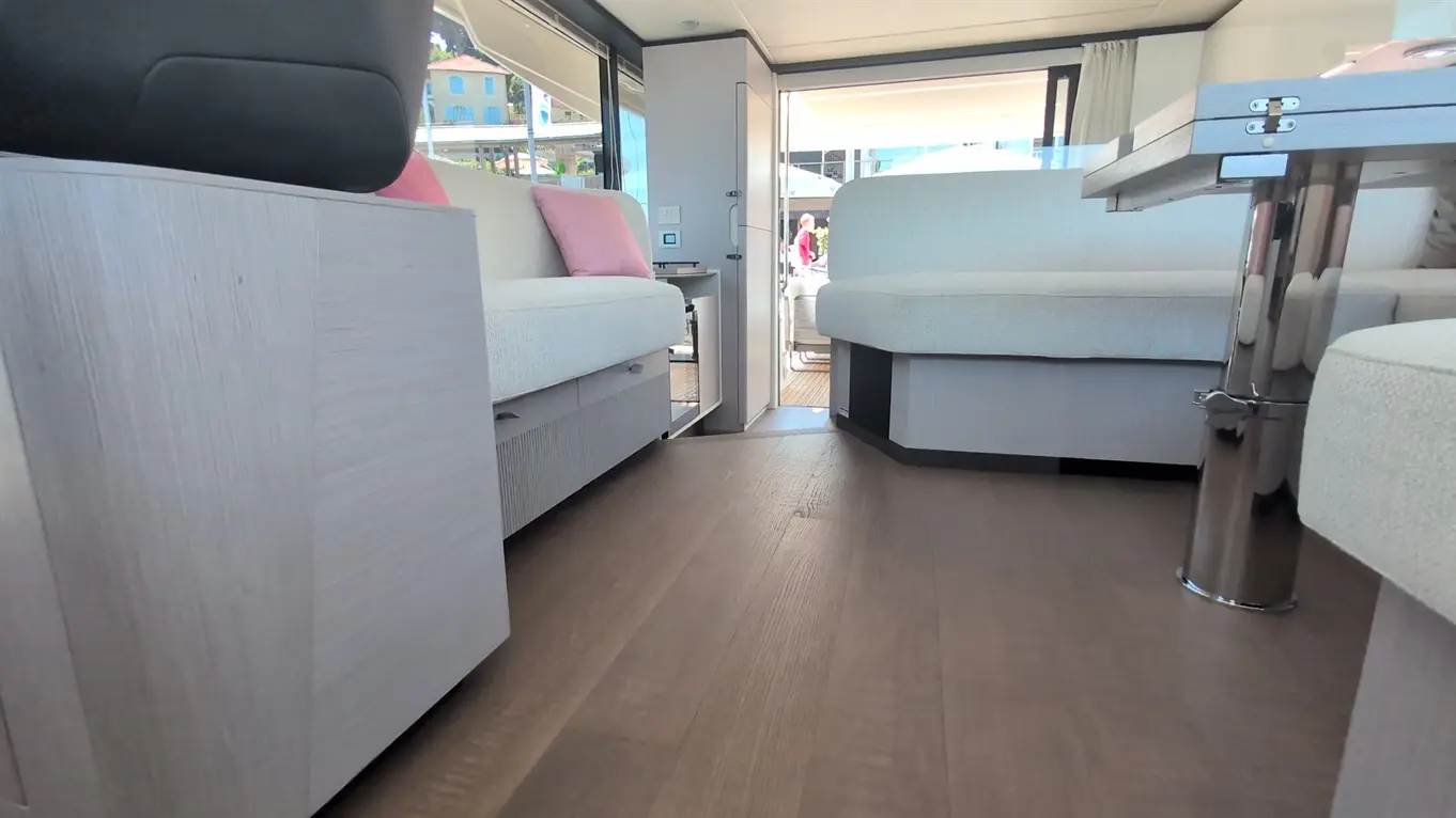 Interior view of a modern boat with light sofas, wooden flooring, and an open space leading to an outdoor area.