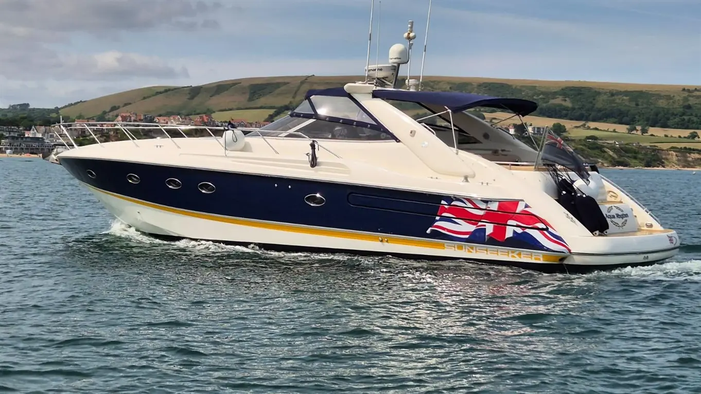 A luxury Sunseeker yacht cruising in calm waters, featuring a British flag decal and scenic green hills in the background.