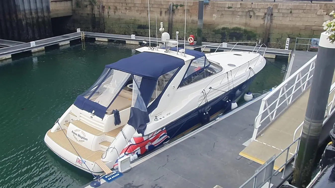 A motorboat named 'Aqua Rhythm' moored at a dock, featuring a blue canopy and Union Jack decoration on the hull.