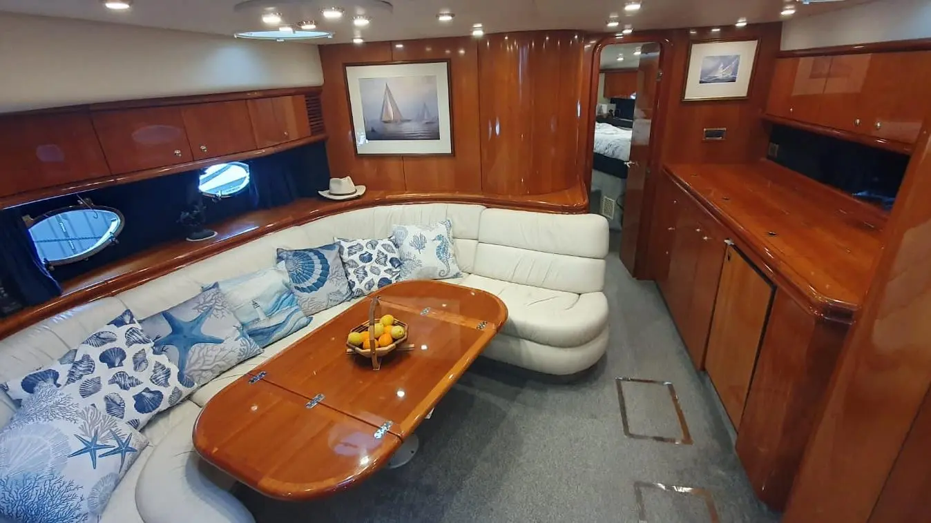 Interior of a yacht featuring leather seating, blue and white cushions, a wooden table with fruit, and marine-themed artwork.