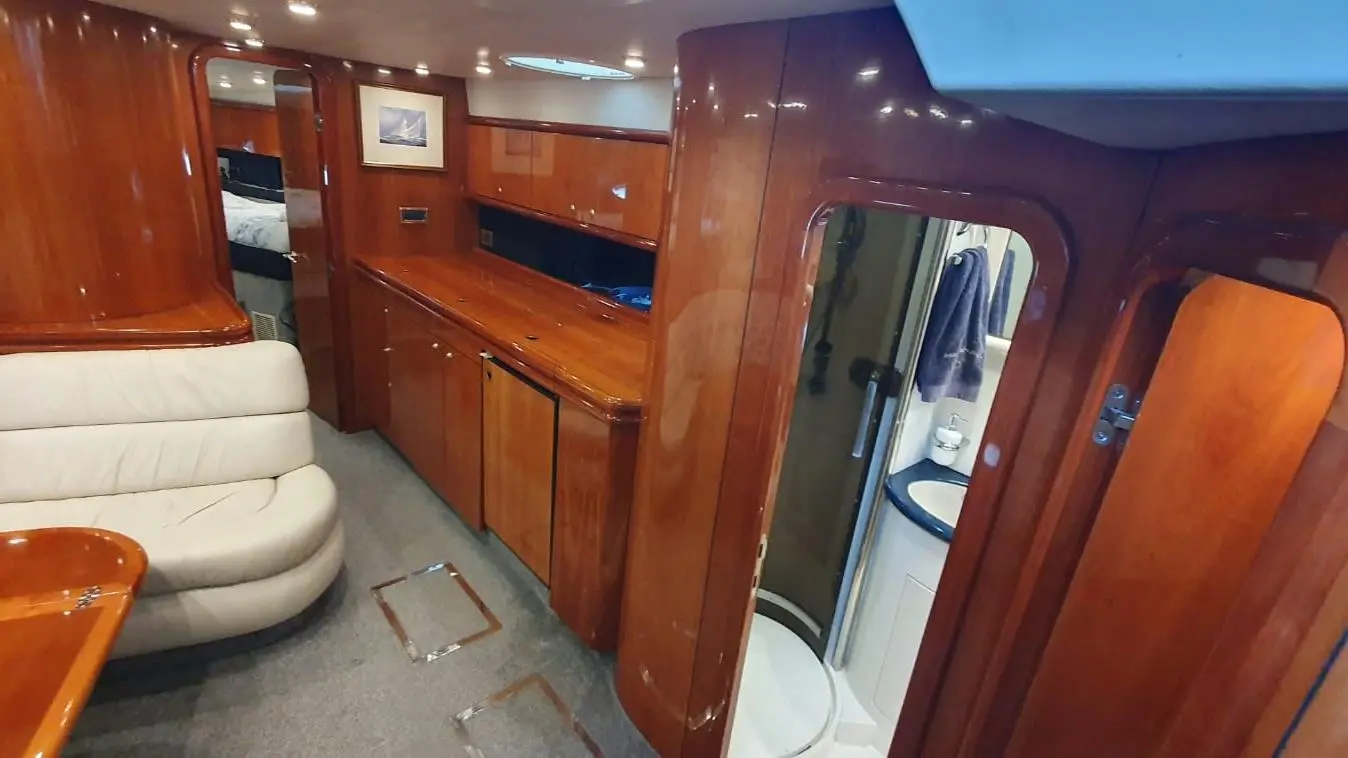 Interior view of a yacht showing a leather sofa, wooden cabinetry, and a bathroom door, with warm lighting and nautical decor.