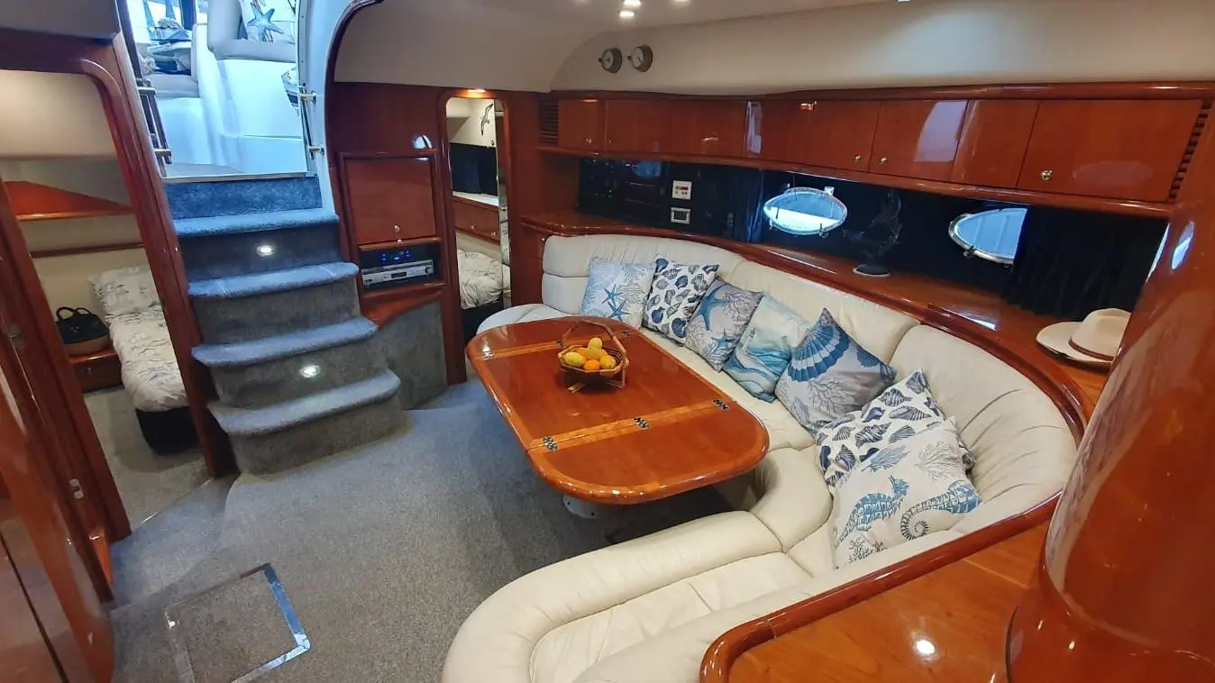 Luxurious boat interior featuring a curved sofa with patterned cushions, a wooden table, and stairs leading to the upper deck.
