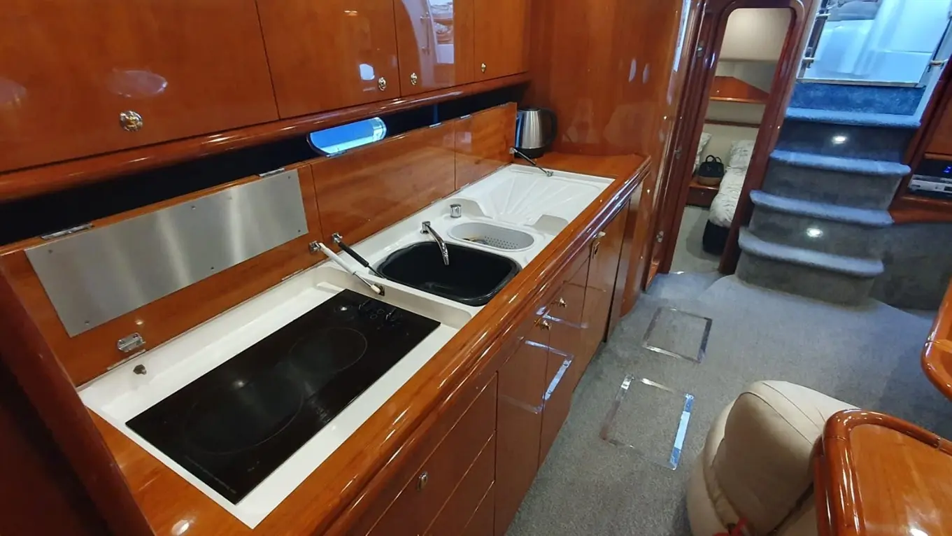 Luxury yacht galley featuring a black stove, sinks, wooden cabinetry, and stairs leading to a lounge area.