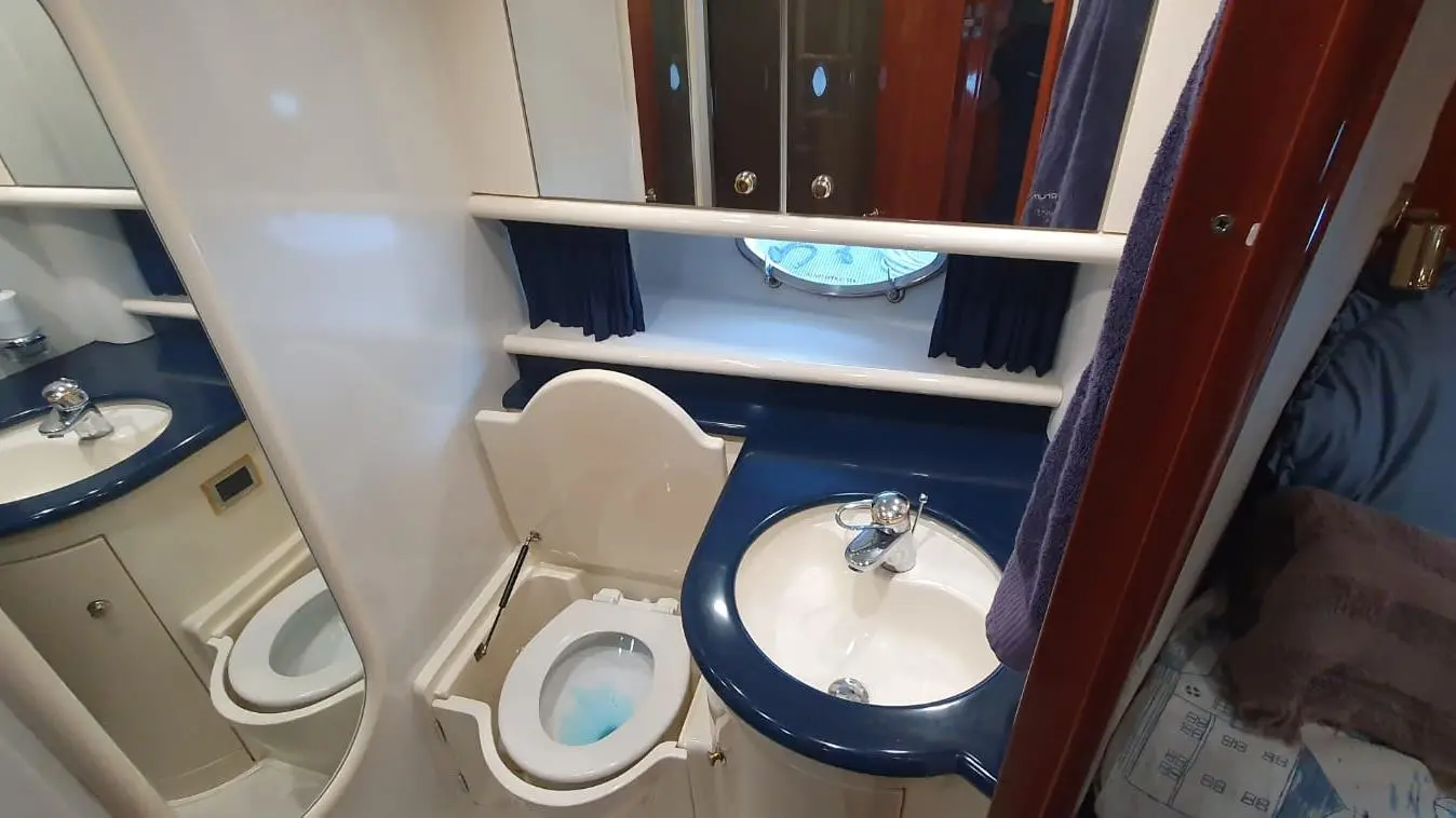 Compact bathroom featuring a sink, toilet, and round mirror, with blue and cream decor and a towel hanging nearby.