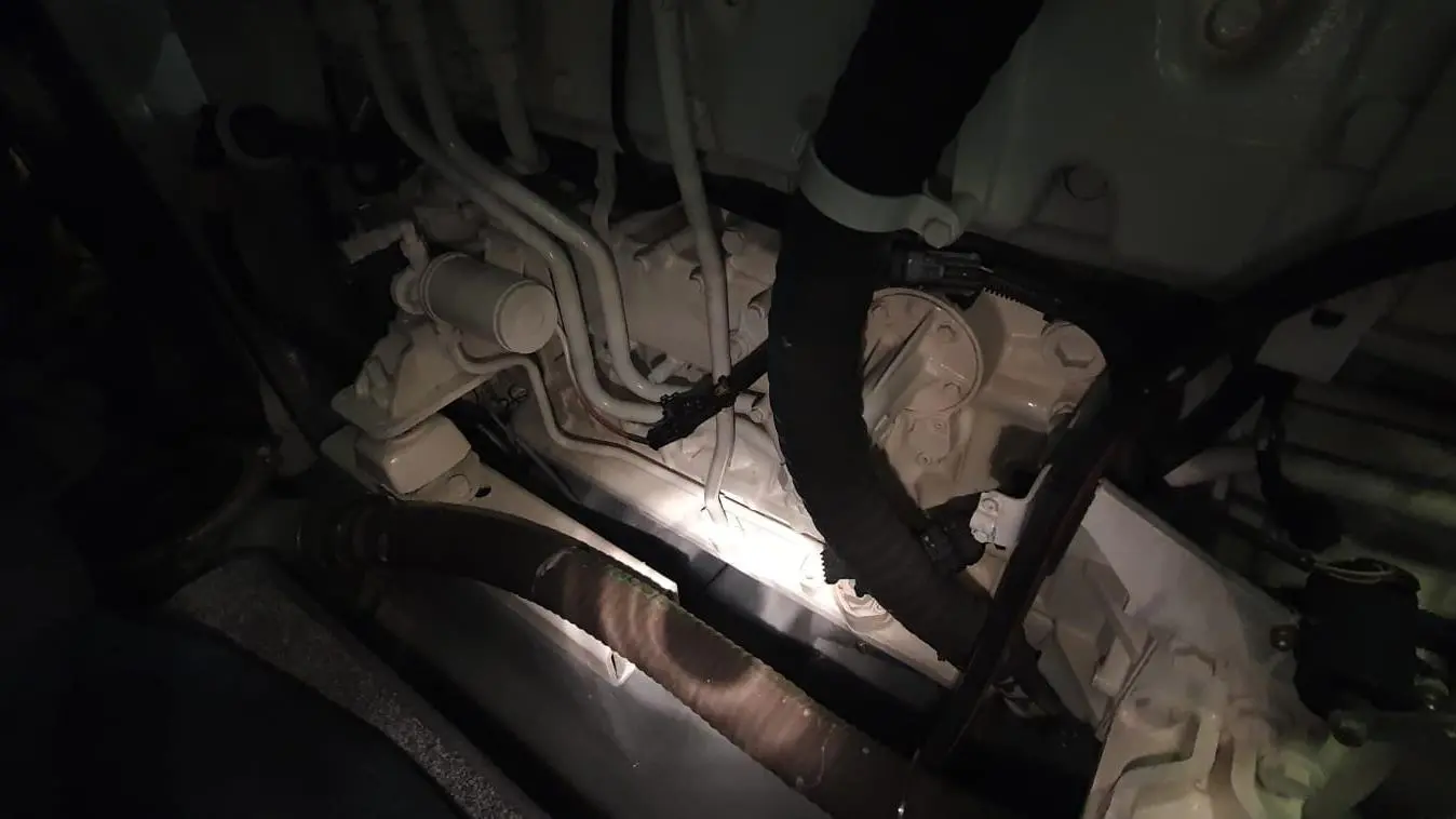 View of a low-lit engine compartment with pipes, hoses, and components, highlighting mechanical details.