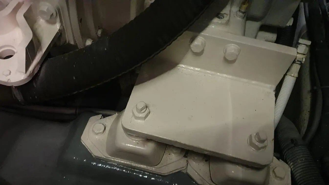 Close-up of an engine mount with bolts and a black hose, showcasing detailed mechanical components and assembly context.