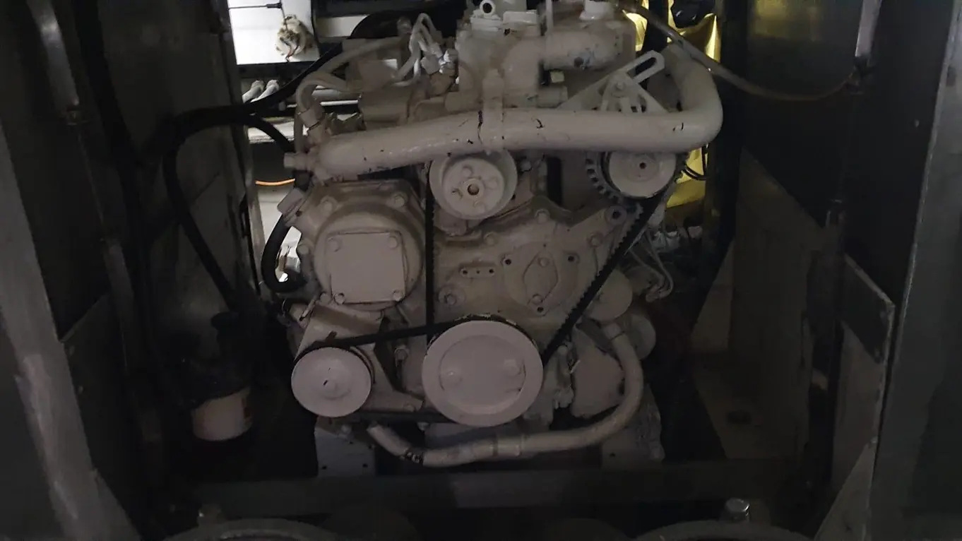 A close-up of a white engine viewed in low light, showcasing pipes, belts, and mechanical components in a vehicle compartment.