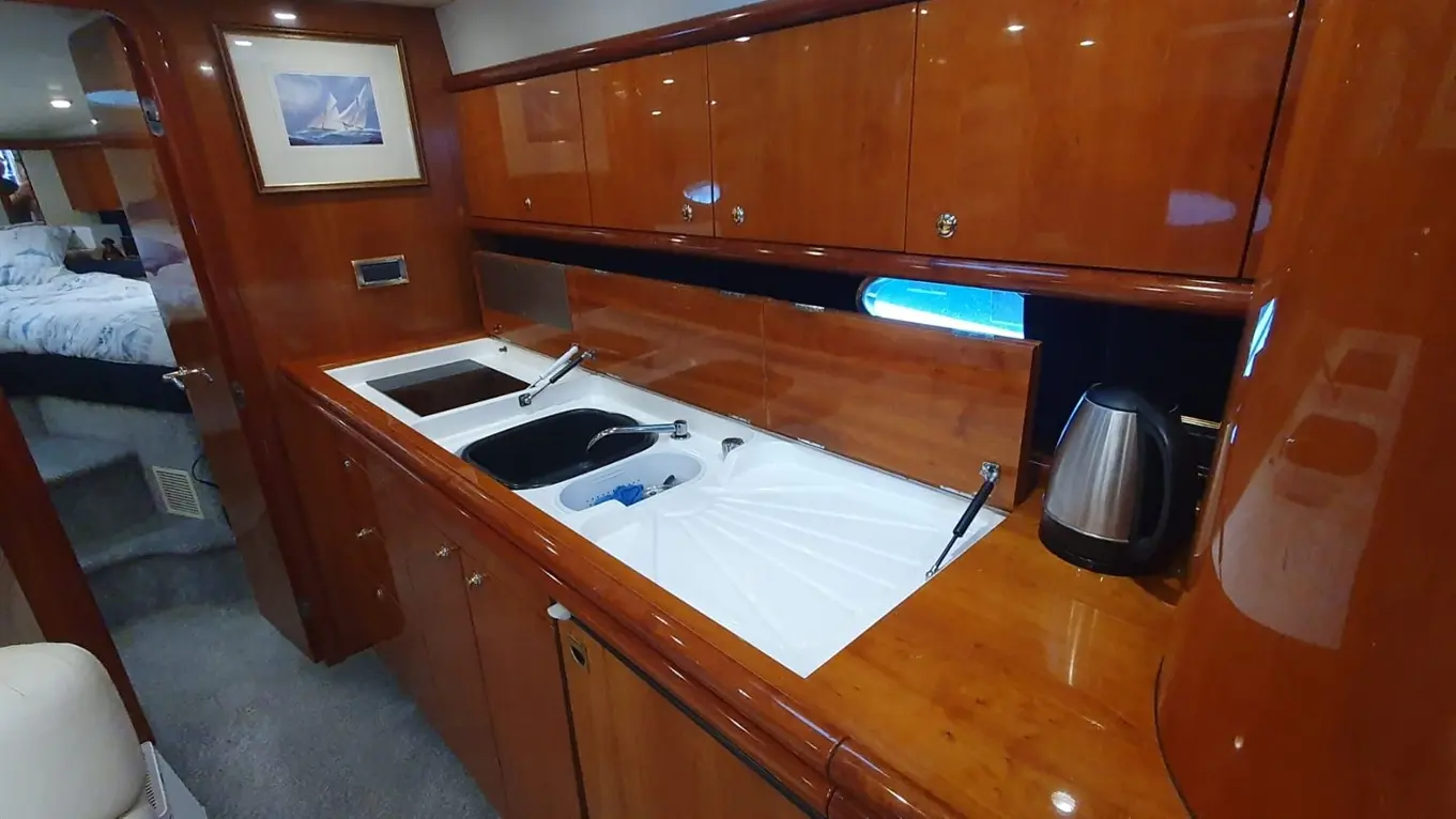 Luxury yacht galley with wooden cabinetry, sink, stovetop, kettle, and a view towards the bedroom through an open door.