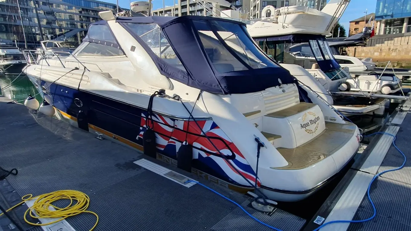 Luxury motorboat named "Aqua Rhythm" docked at a marina, featuring a British flag design and surrounded by other vessels.