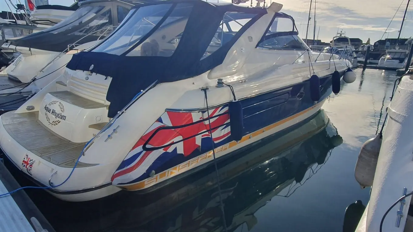 A motorboat named 'Aqua Rhythm' with a Union Jack design, moored in a marina, with reflections in the water.