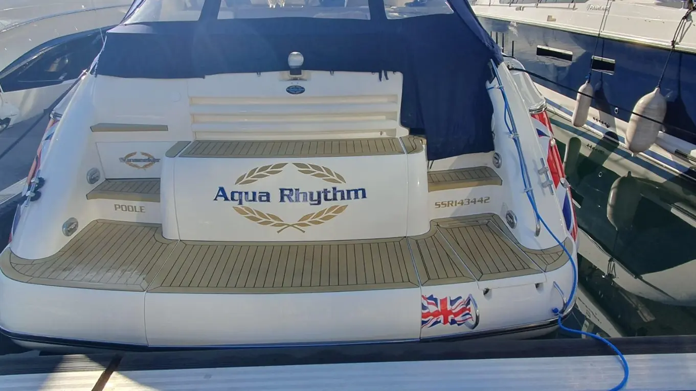Boat named "Aqua Rhythm" docked at a marina, featuring a British flag and the name "Poole" on its stern.