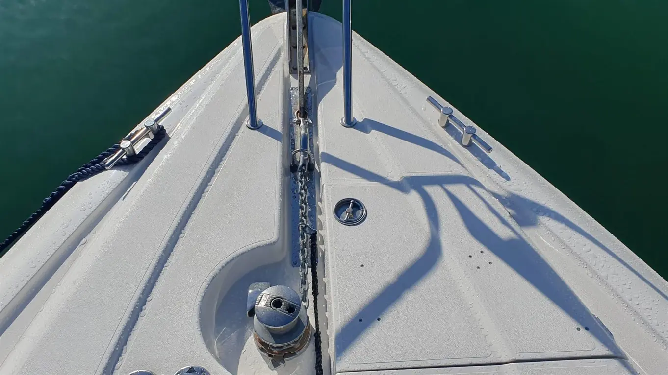 Bow of a boat showing a white deck, stainless steel fittings, an anchor chain, and green water below.
