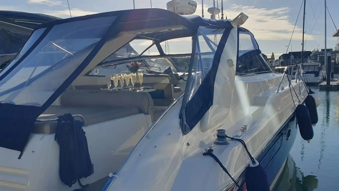 A luxury boat at a marina, featuring a clear canopy, lounge seating, and a tray with champagne flutes on the deck.