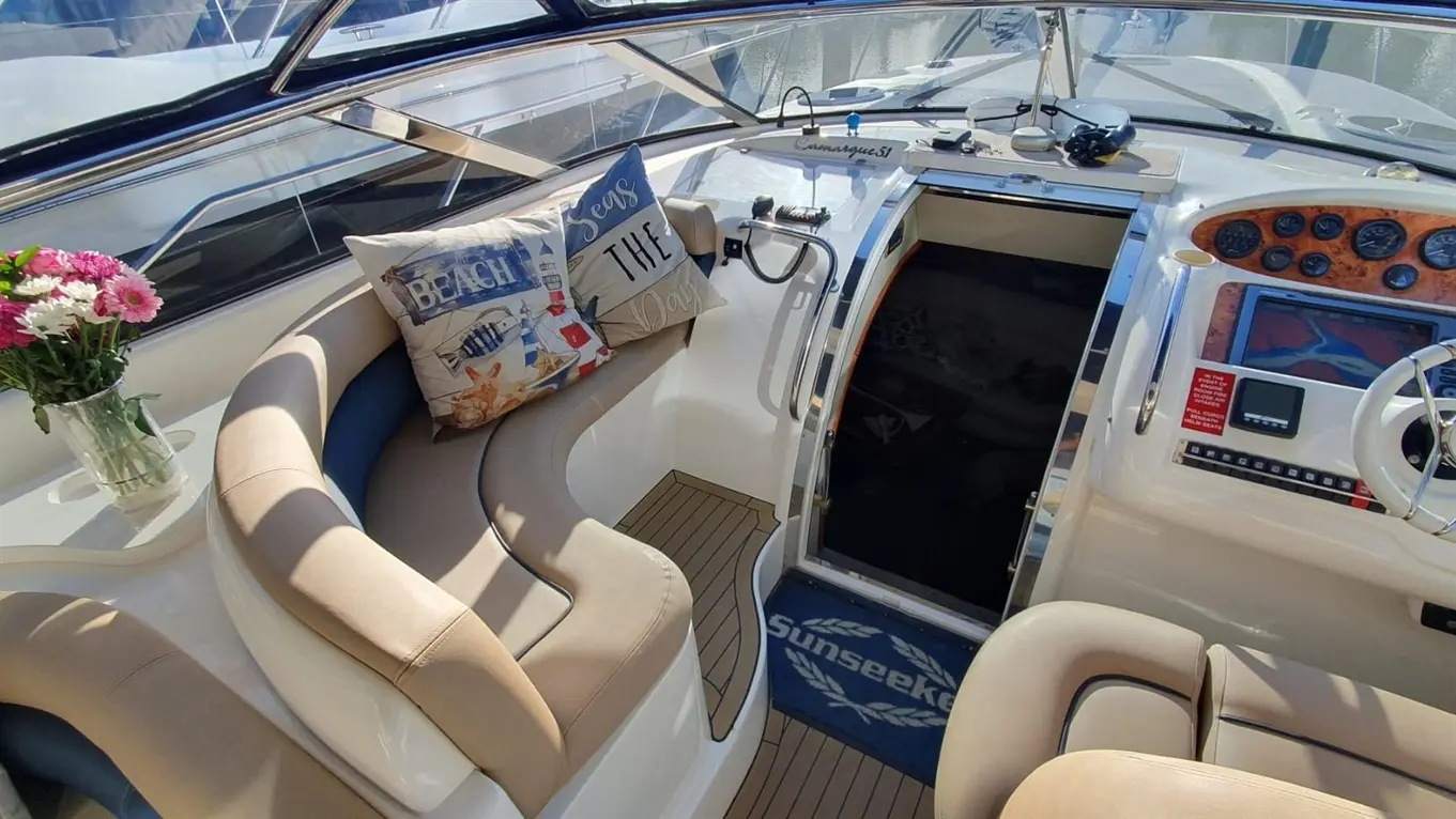 Interior of a luxury motorboat featuring a dashboard, two decorative cushions, a flower vase, and a carpet marked "Sunseeker.