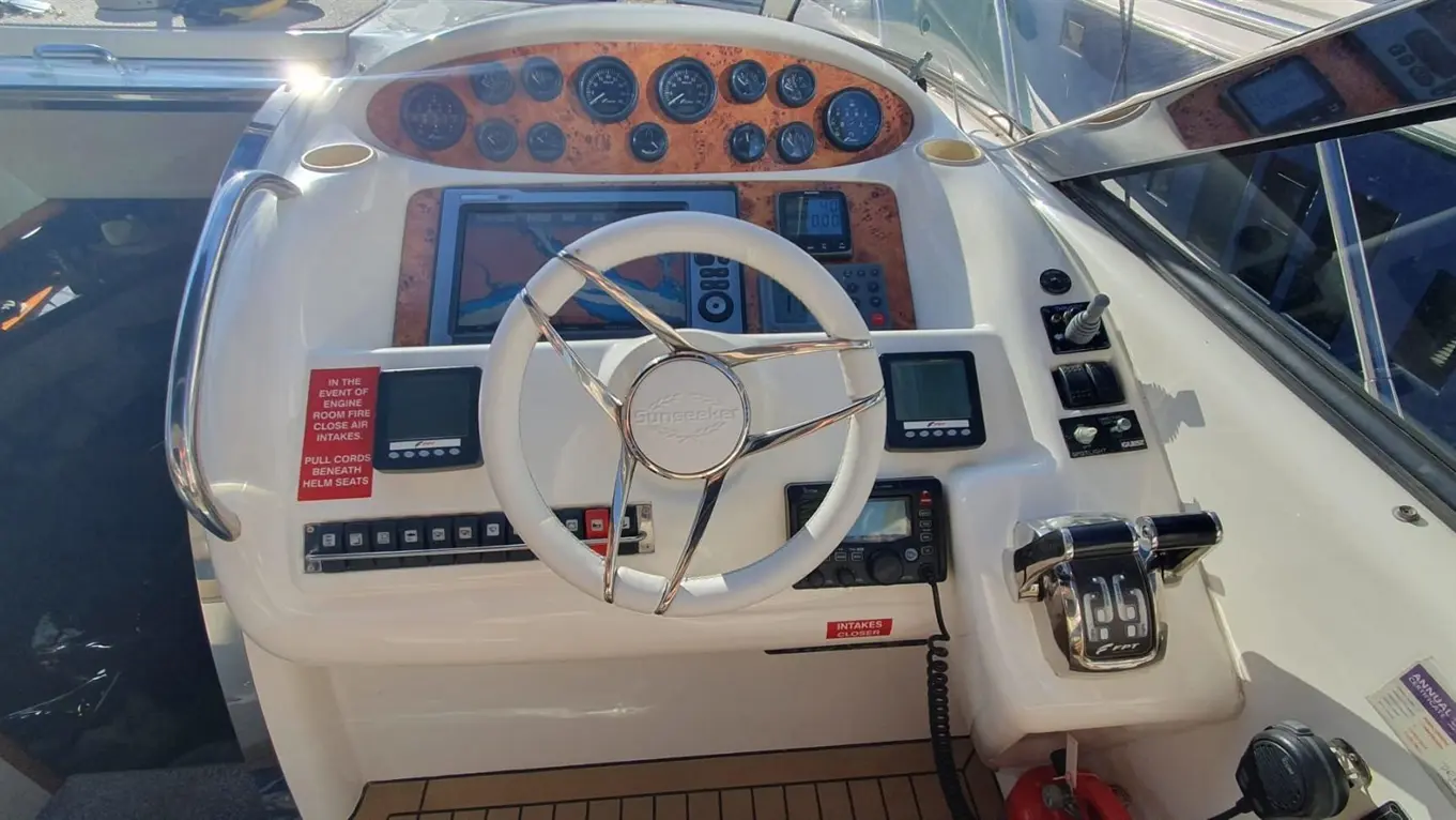 Boat dashboard featuring a steering wheel, gauges, navigation screen, and safety instructions for engine room use.