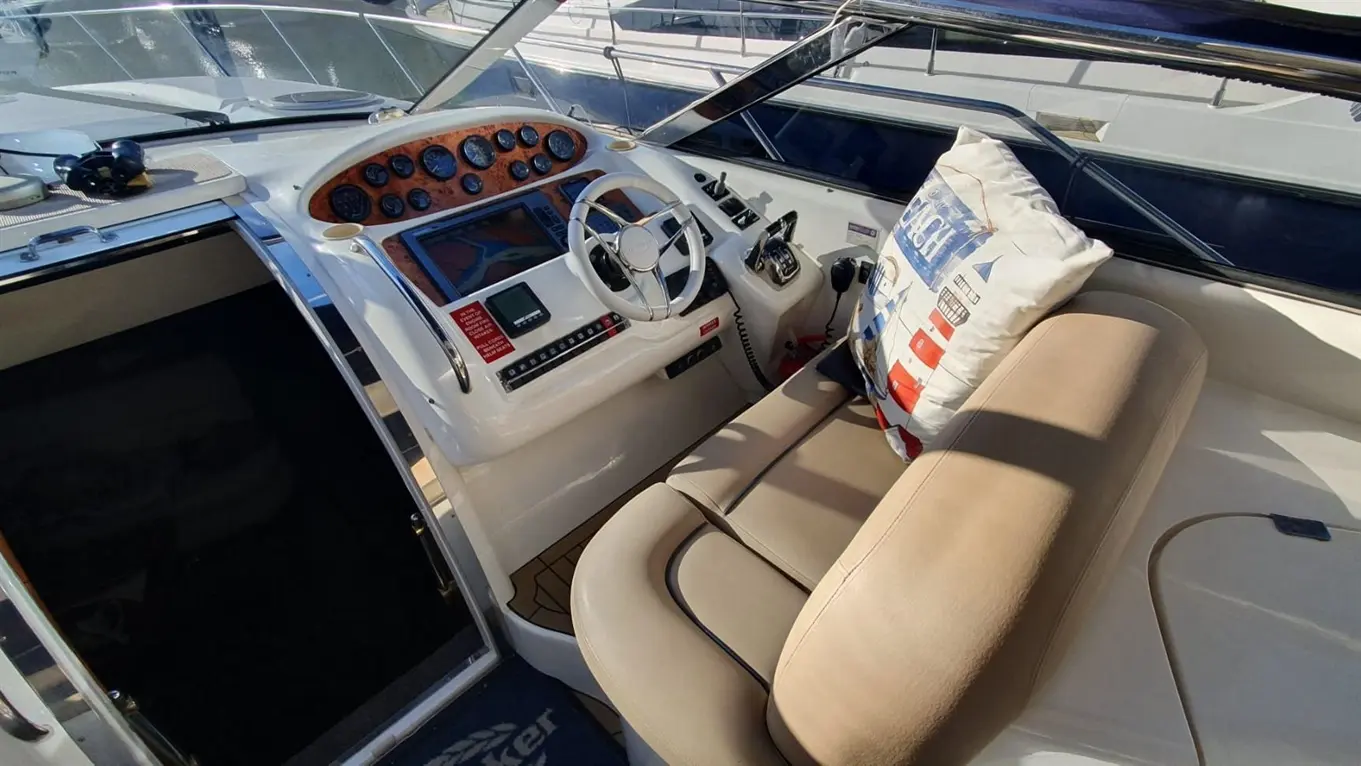 A luxury boat's cockpit featuring a steering wheel, control panel, and a cushioned seat with a decorative lighthouse pillow.