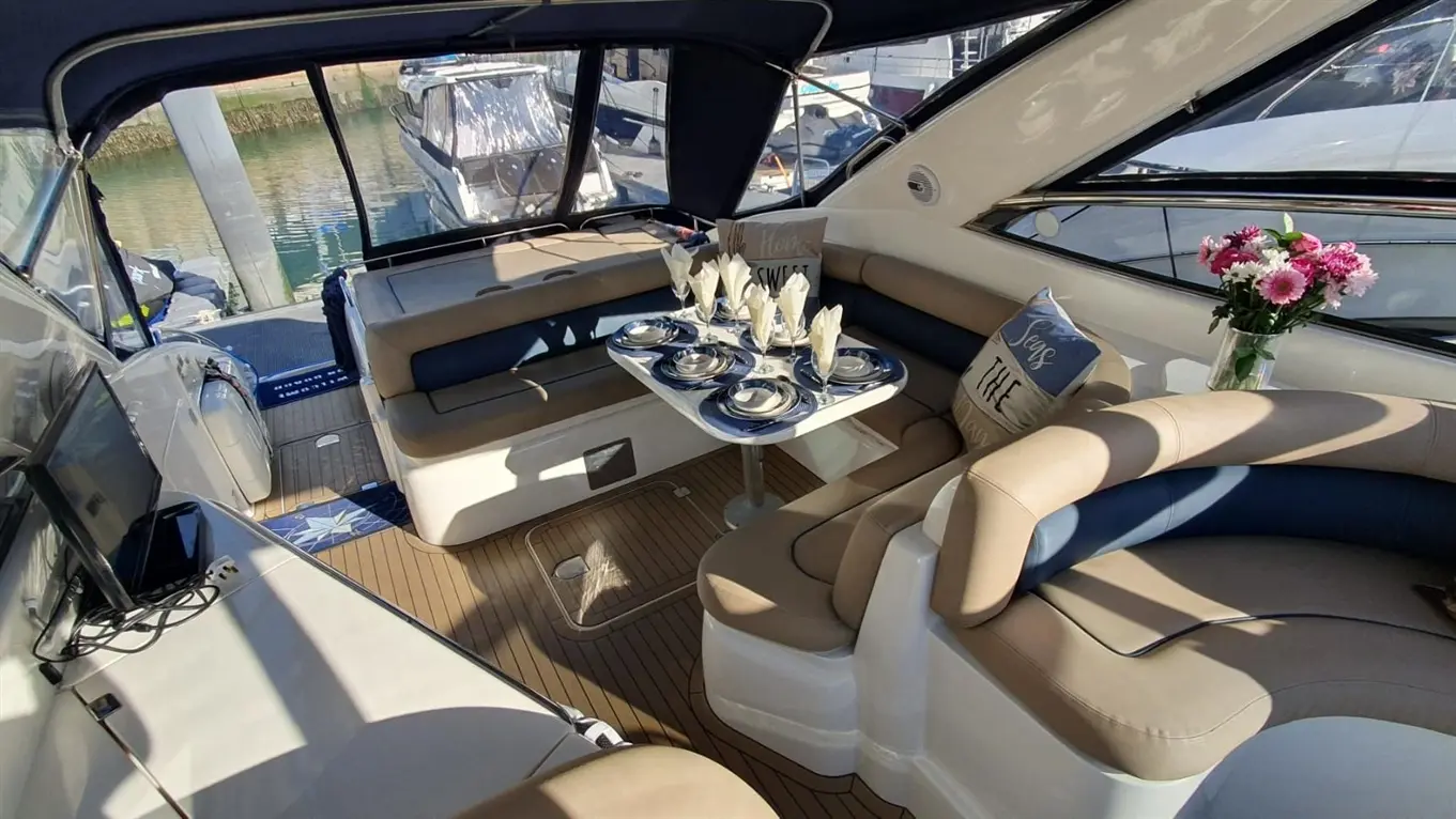 Interior of a boat featuring a dining area with a table set, plush seating, and a vase of flowers by the window.