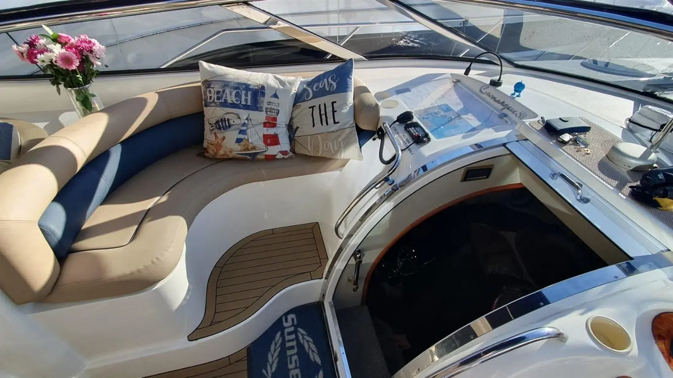 Interior of a boat featuring a comfortable seating area, decorative cushions, a steering console, and a floral arrangement.
