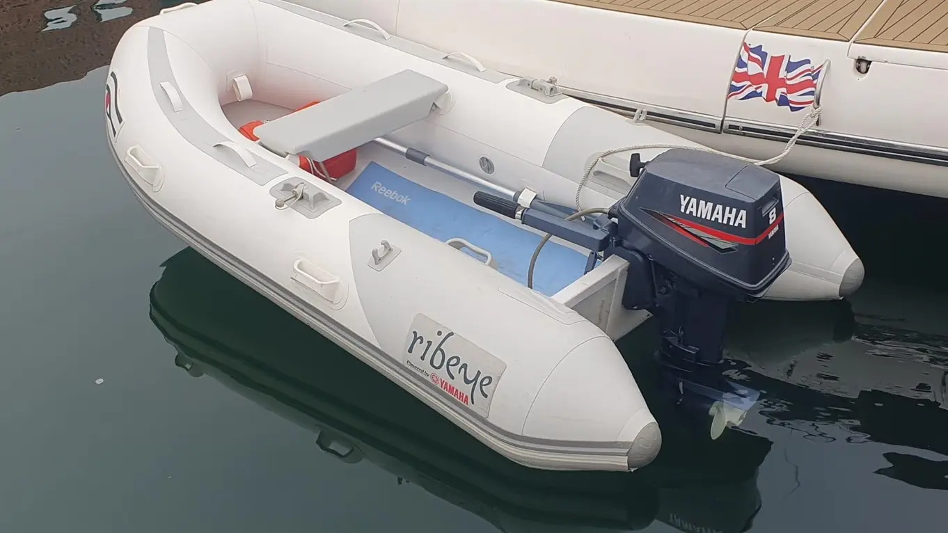 A white rib boat with a Yamaha engine is docked, displaying a British flag and blue Reebok mat inside.
