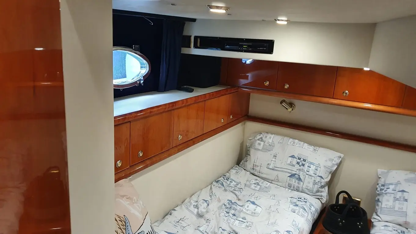 Interior of a boat cabin featuring two single beds with nautical-themed bedding, a porthole, and wooden storage cabinets.