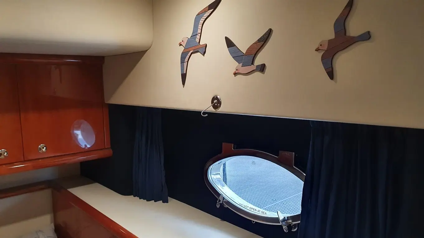 Interior of a boat cabin featuring wooden bird decorations, a round porthole window, and a dark curtain beside a polished surface.