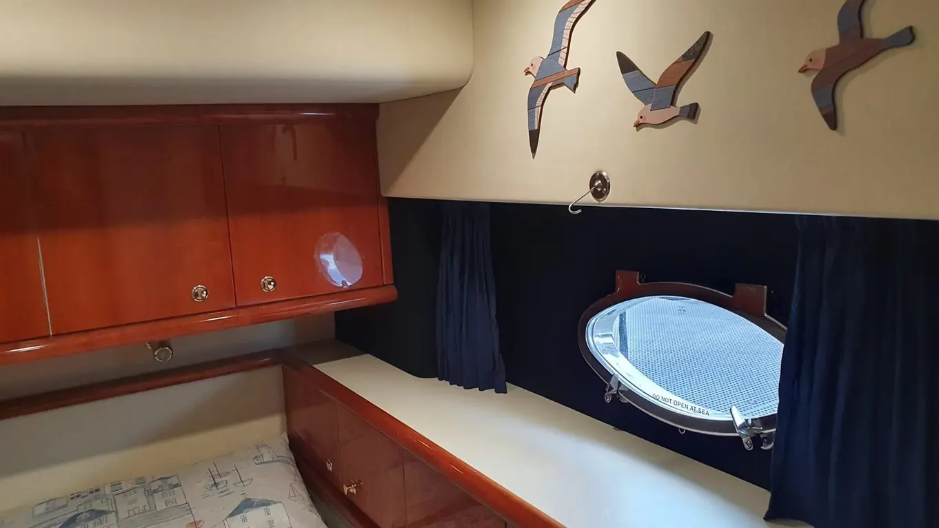Interior of a yacht cabin featuring wooden cabinets, blue curtains, decorative wooden birds, and an oval porthole window.