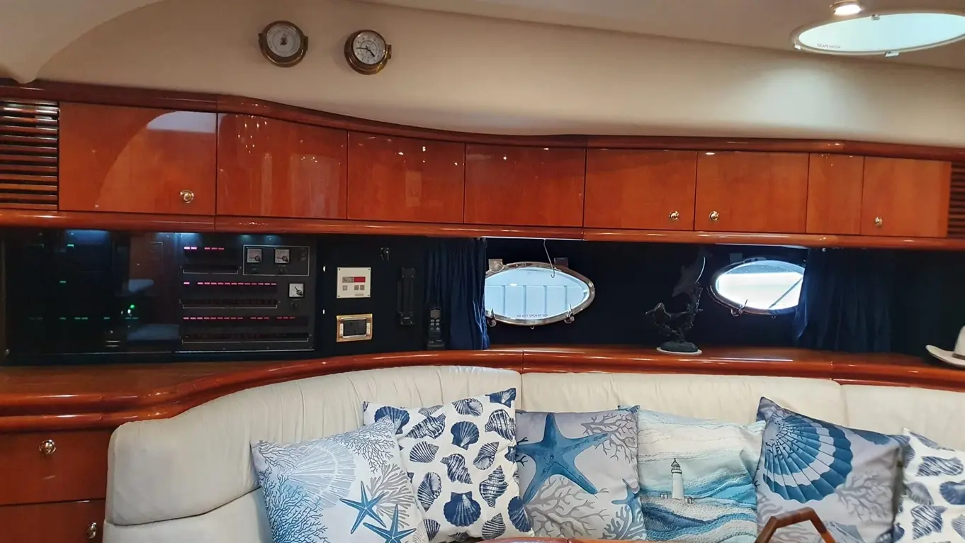 Interior of a yacht featuring plush seating, nautical-themed cushions, control panel, and a fruit basket on a wooden table.
