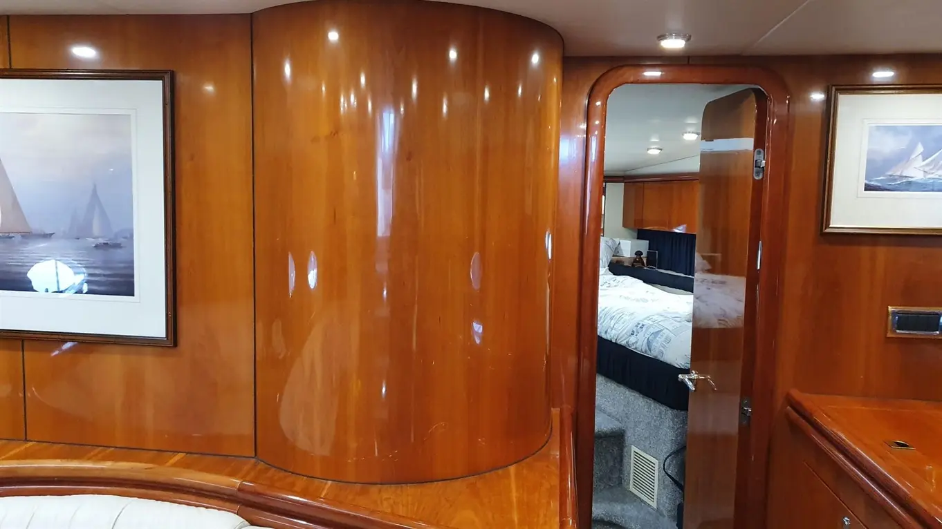 Interior of a yacht featuring polished wood paneling, a framed sailing painting, and an open door leading to a bedroom.