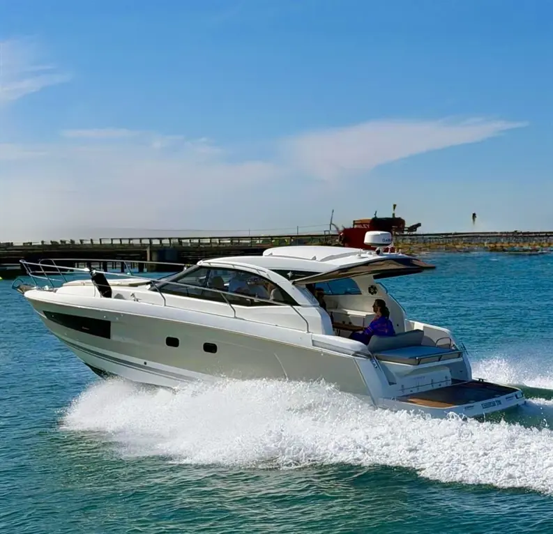 A sleek white motorboat speeds through clear blue waters, with a person seated at the helm against a sunny sky.