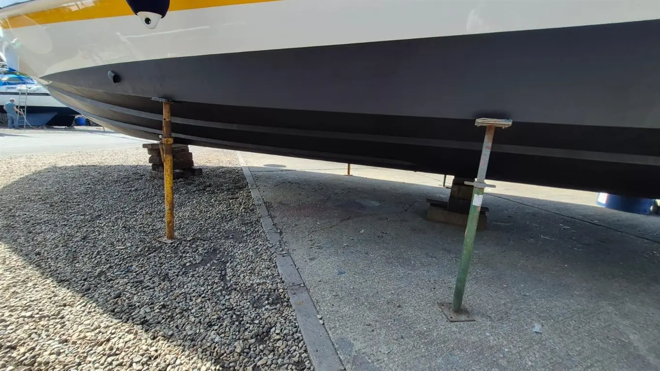 A boat supported by metal struts on a gravel surface, showcasing a view of its hull and the surrounding marina.