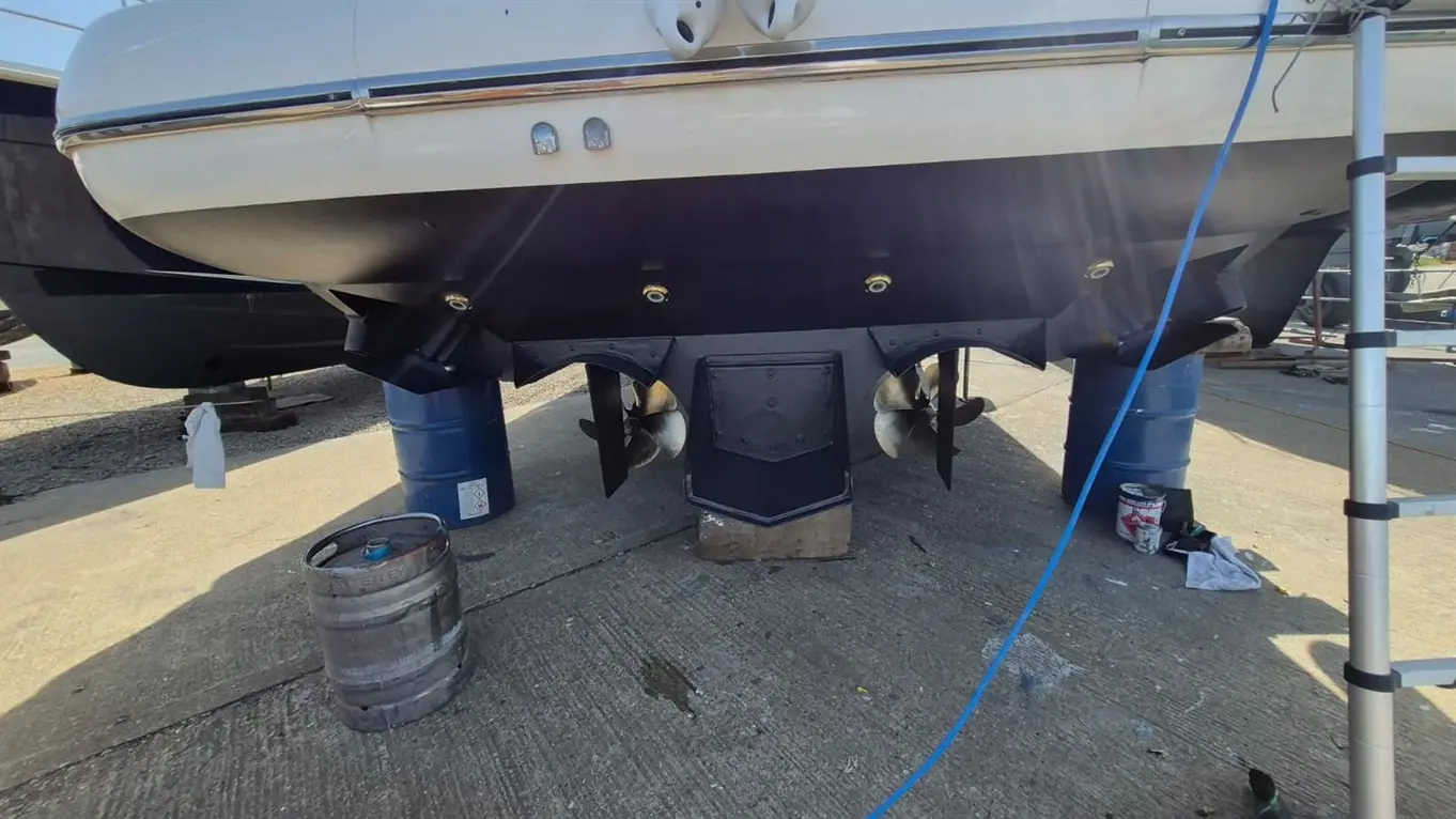 Powerboat on blocks for maintenance, featuring dual propellers and British flag. Tools and equipment scattered nearby.