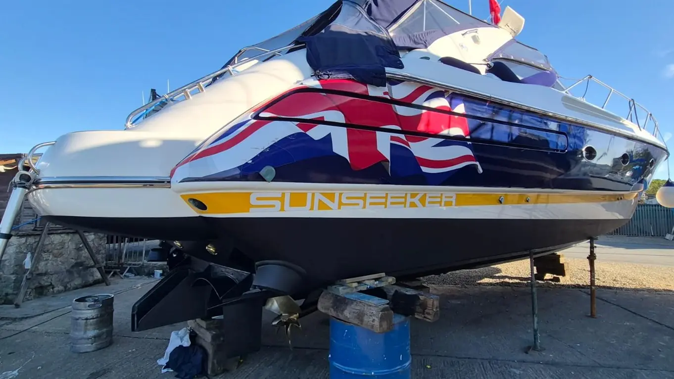 A luxury Sunseeker yacht on stands, featuring a Union Jack design and set against a clear blue sky in a marina.