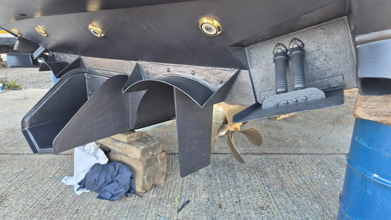 View of a boat's underside, showcasing two jet nozzle mounts, a propeller, and black spray rails on a concrete surface.